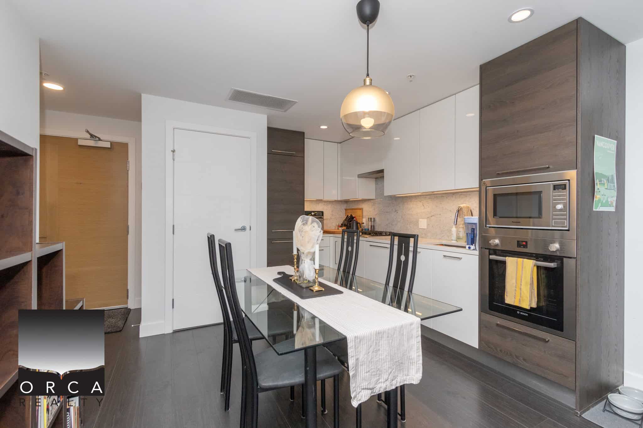 Contemporary modern kitchen interior with white cabinets, wood accents, stainless steel appliances, and a glass dining table in a sleek apartment. Perfect for enjoying meals in style.