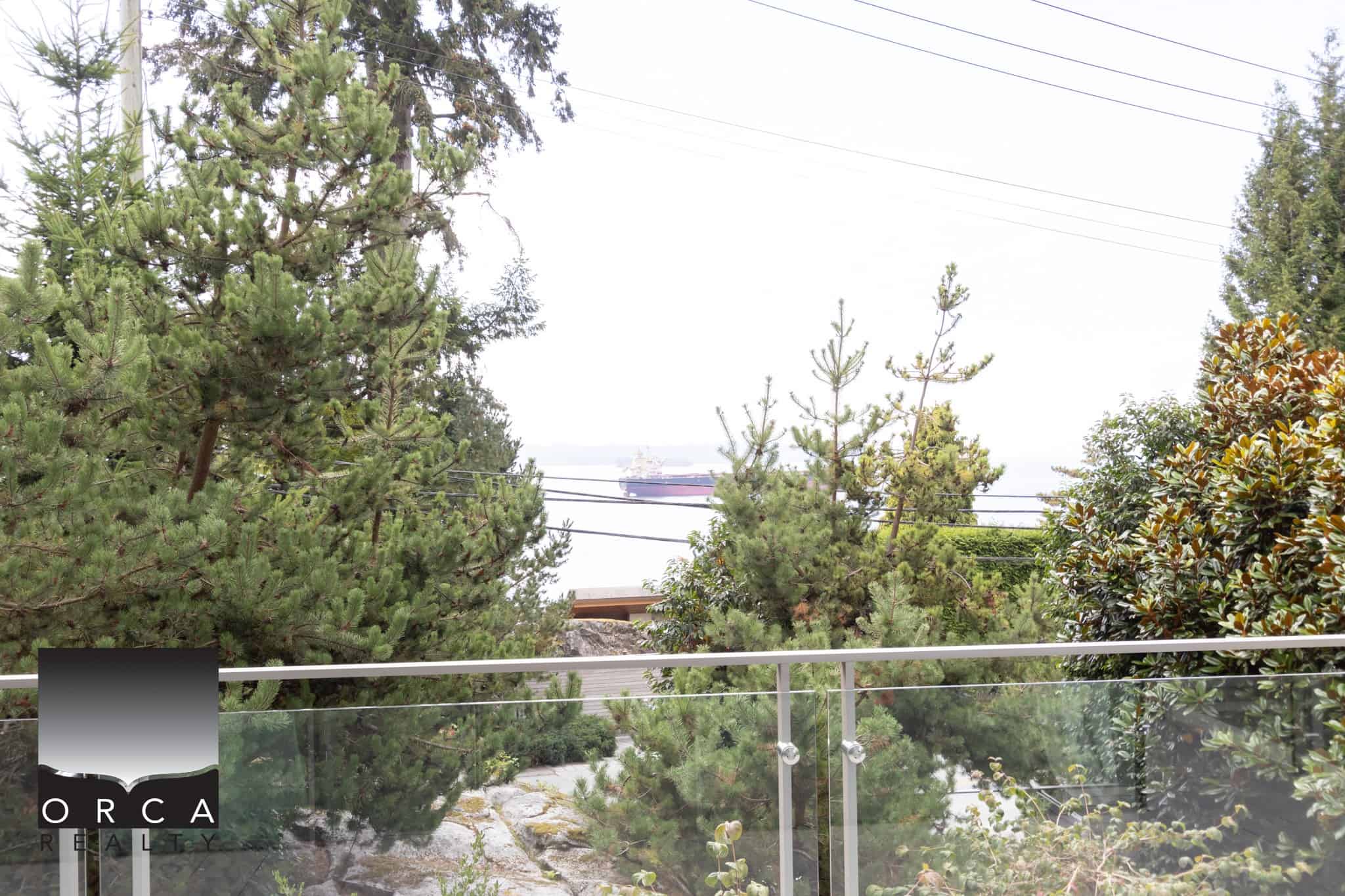 Pontevedra Harbour view with lush green trees and a ship in the background, captured from a modern balcony with glass railing, offering a serene coastal living experience in Vancouver.