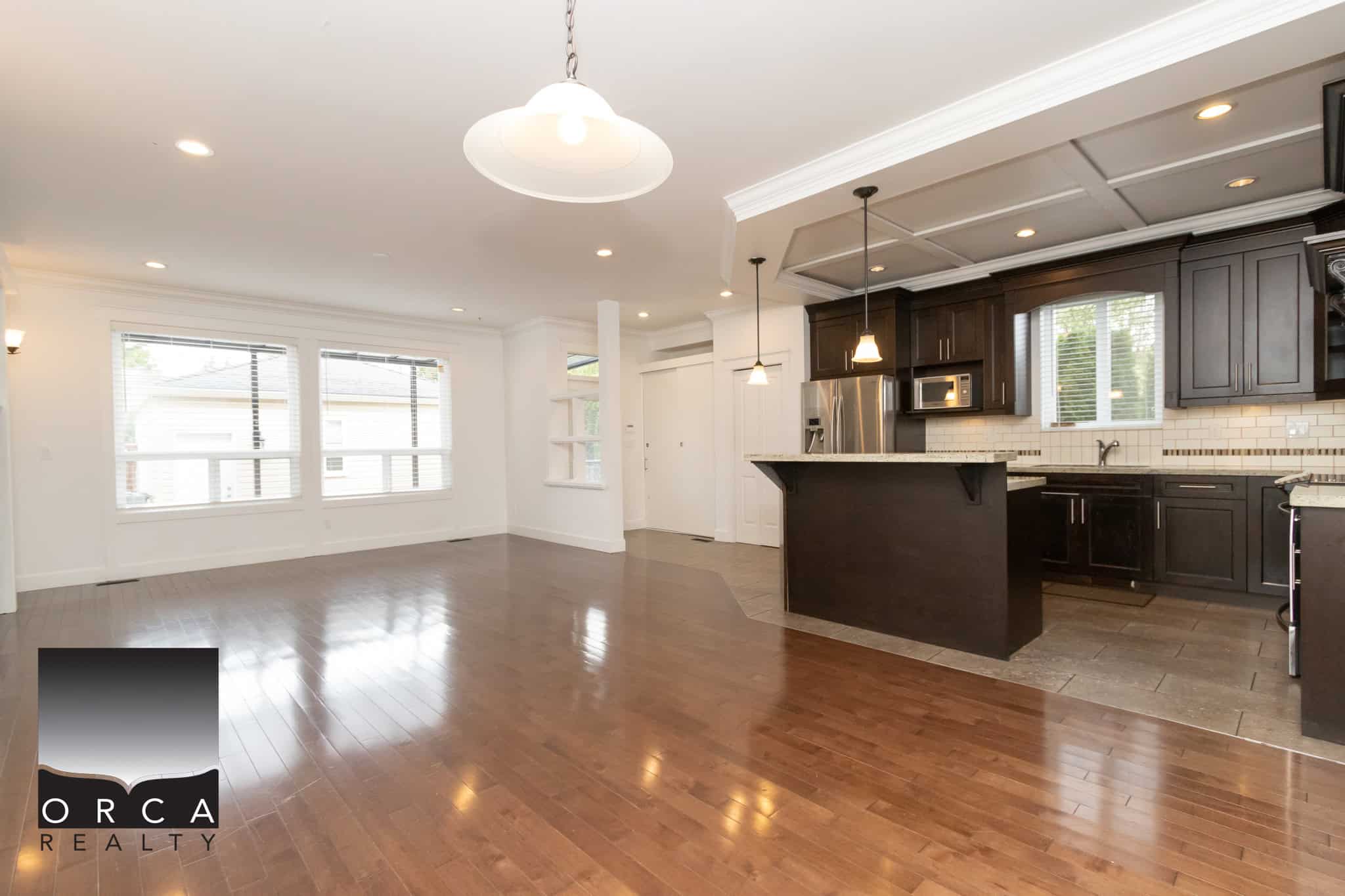 Bright open-concept living room and kitchen in a modern home, featuring hardwood floors, large windows, dark cabinetry, and a stylish kitchen island, ideal for family living and entertaining.