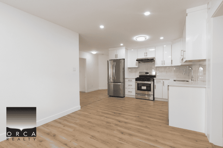 Stainless steel refrigerator and oven in modern white kitchen with wood flooring, bright lighting, and ample cabinetry, ideal for Vancouver real estate listings.