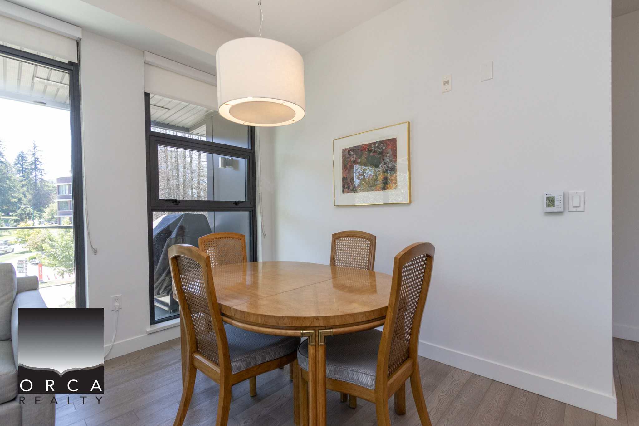 Modern dining area with wooden table and chairs, large windows providing natural light, in a contemporary condo at Orca Realty Inc., Vancouver real estate specialists.