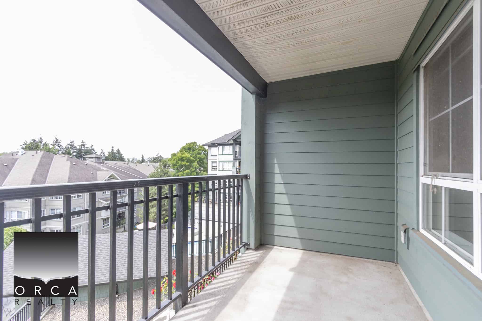 Balcony of a modern residential apartment with green siding, black metal railing, view of surrounding rooftops and trees, ideal for outdoor relaxation in Vancouver BC.