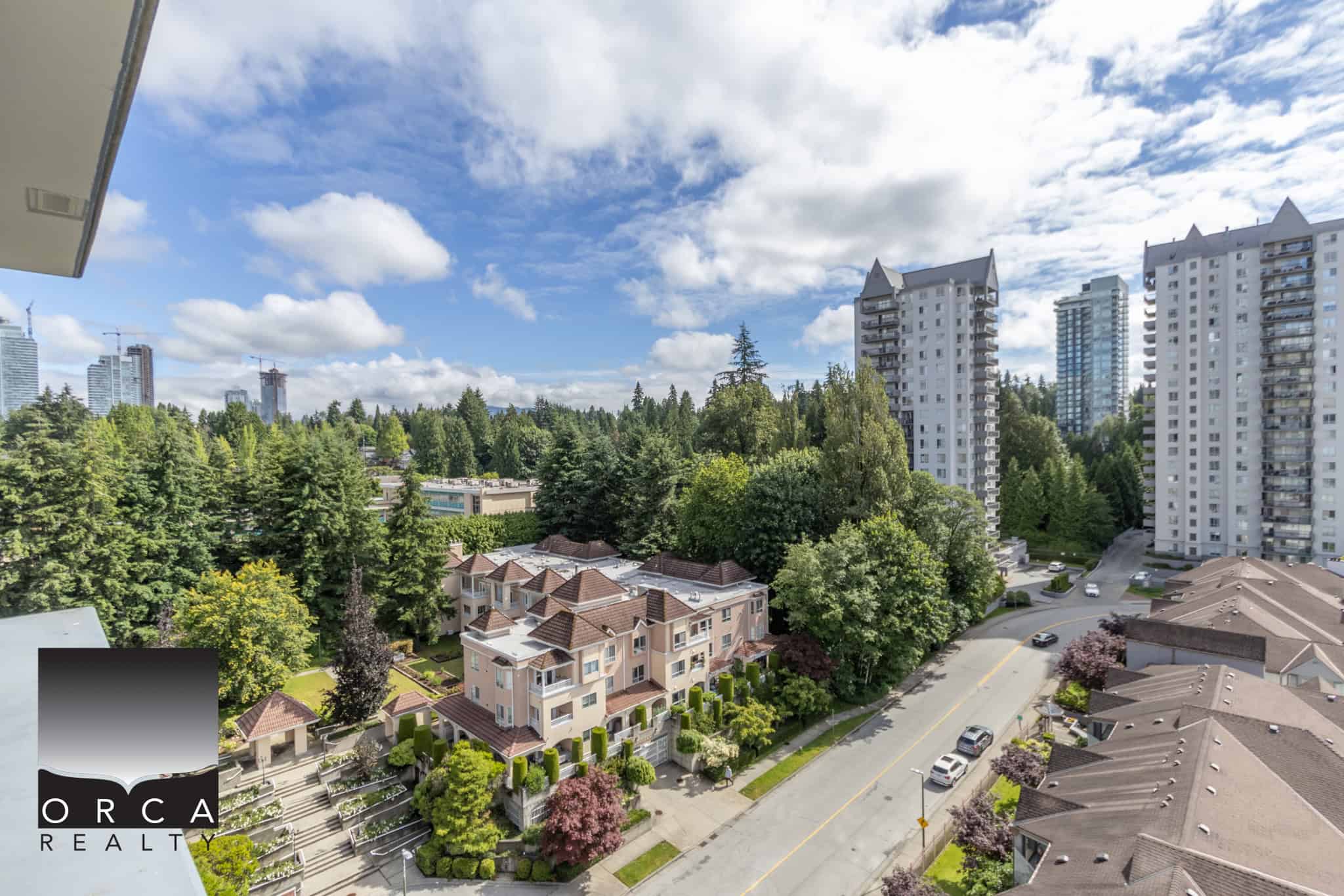 Bright Vancouver skyline view with residential buildings, lush green trees, and a clear blue sky, showcasing prime Vancouver real estate opportunities with Orca Realty Inc. SEO-friendly image.