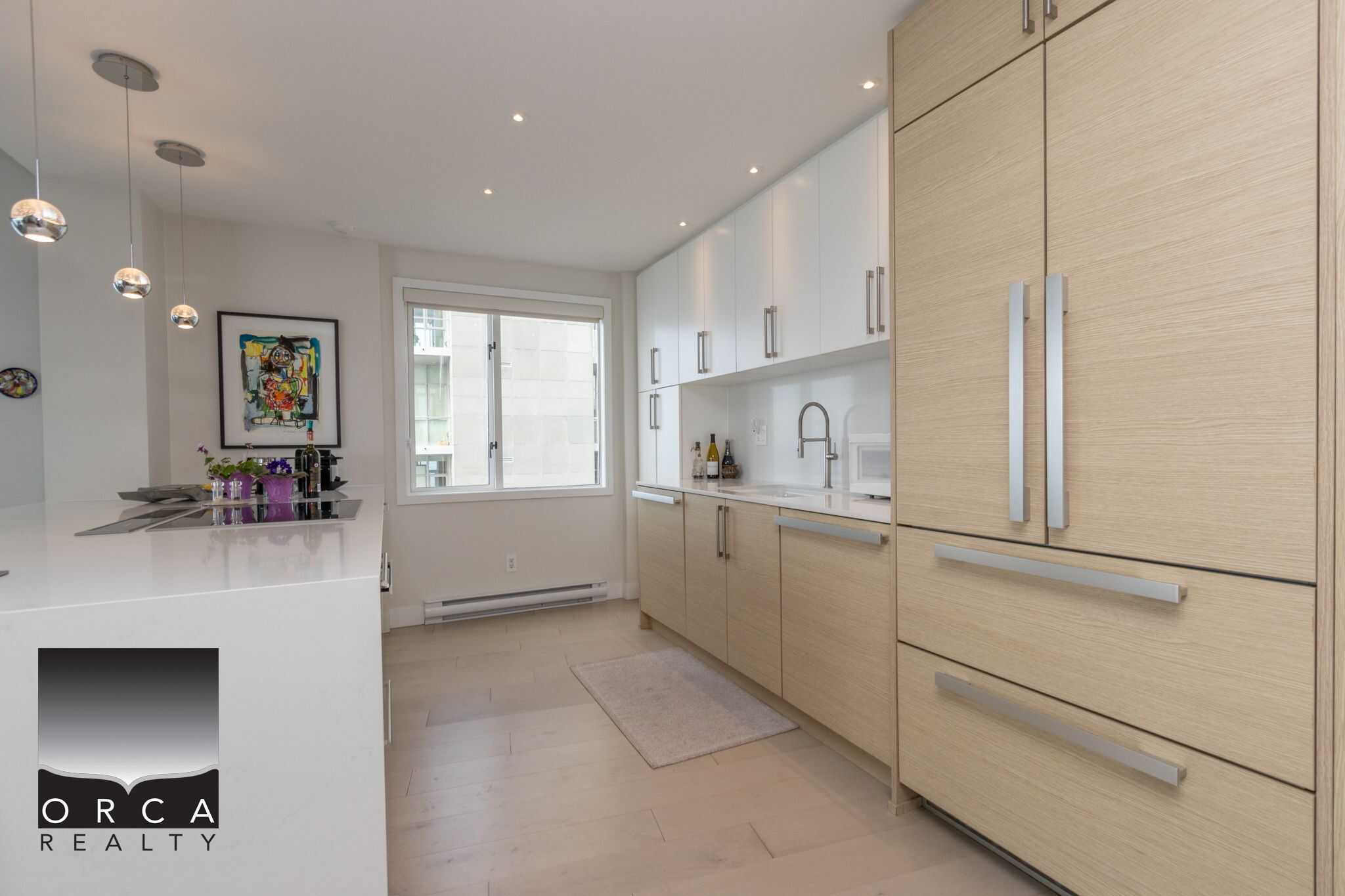 Modern kitchen interior with minimalist light wood cabinets and white countertops, featuring stainless steel handles, a large window, and elegant pendant lighting, ideal for Vancouver real estate buyers.