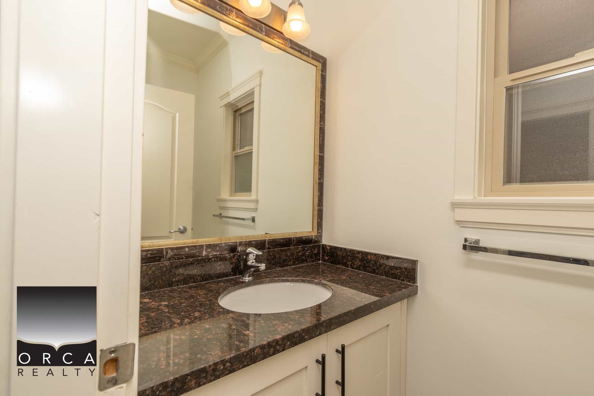 Modern bathroom vanity with dark granite countertop and white cabinetry, featuring a mirror and window for natural light, perfect for Vancouver Island real estate.