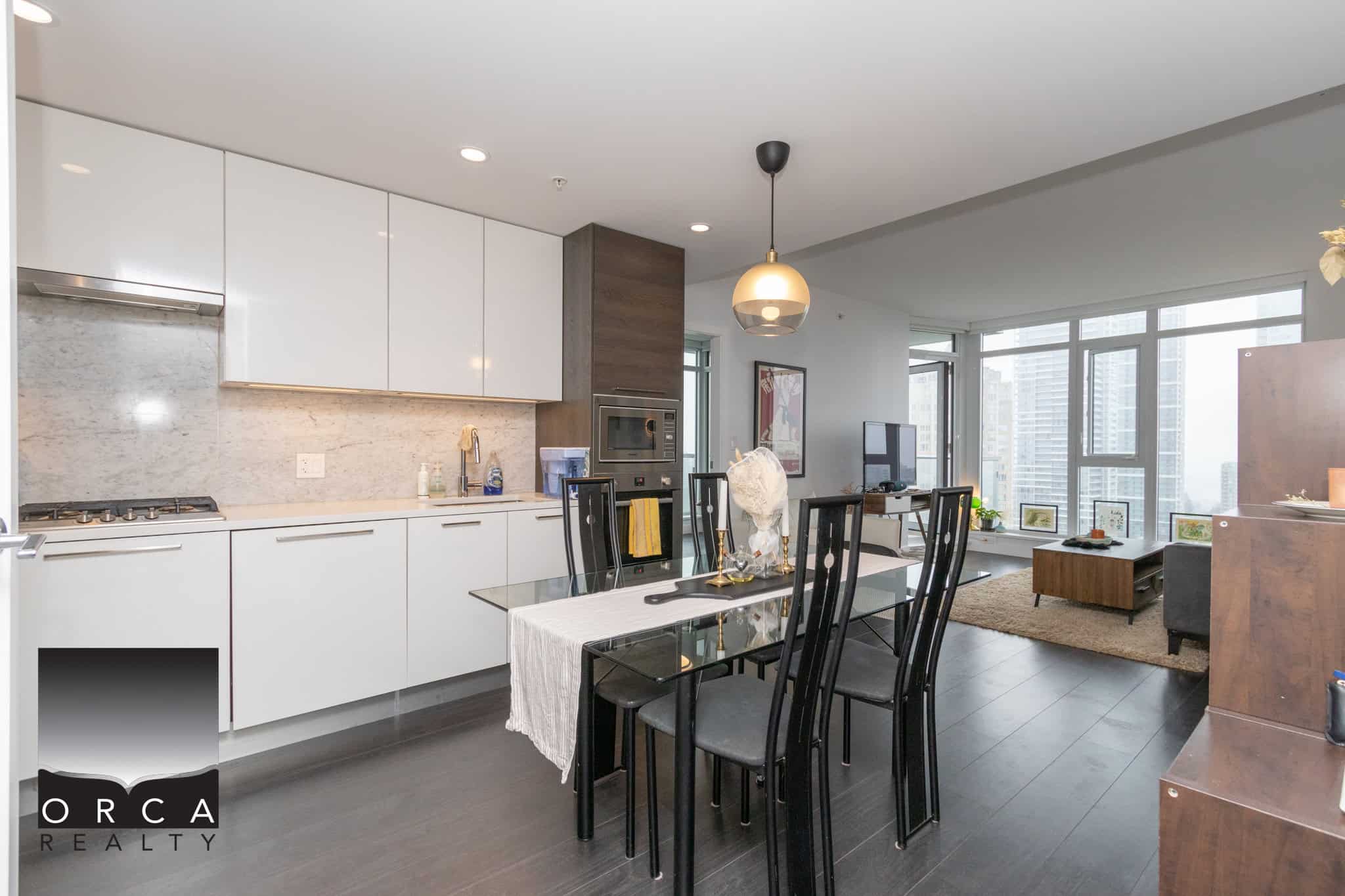 Modern high-rise condo interior with open kitchen and living area, featuring minimalist white cabinetry, sleek dining table, and panoramic city views, ideal for urban living.