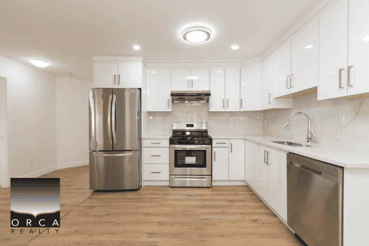 Modern white kitchen with stainless steel appliances, including refrigerator, stove, and dishwasher, in a new residential property listed by Orca Realty Inc.
