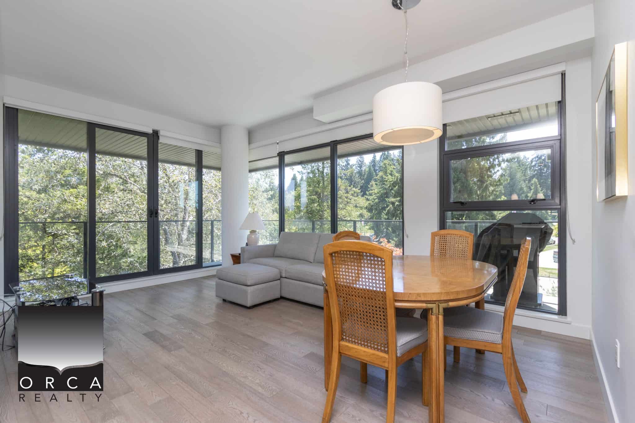 Bright, spacious living room with large windows, overlooking lush trees, and featuring modern furniture, perfect for relaxing and entertaining in a Vancouver-area home listed by Orca Realty Inc.