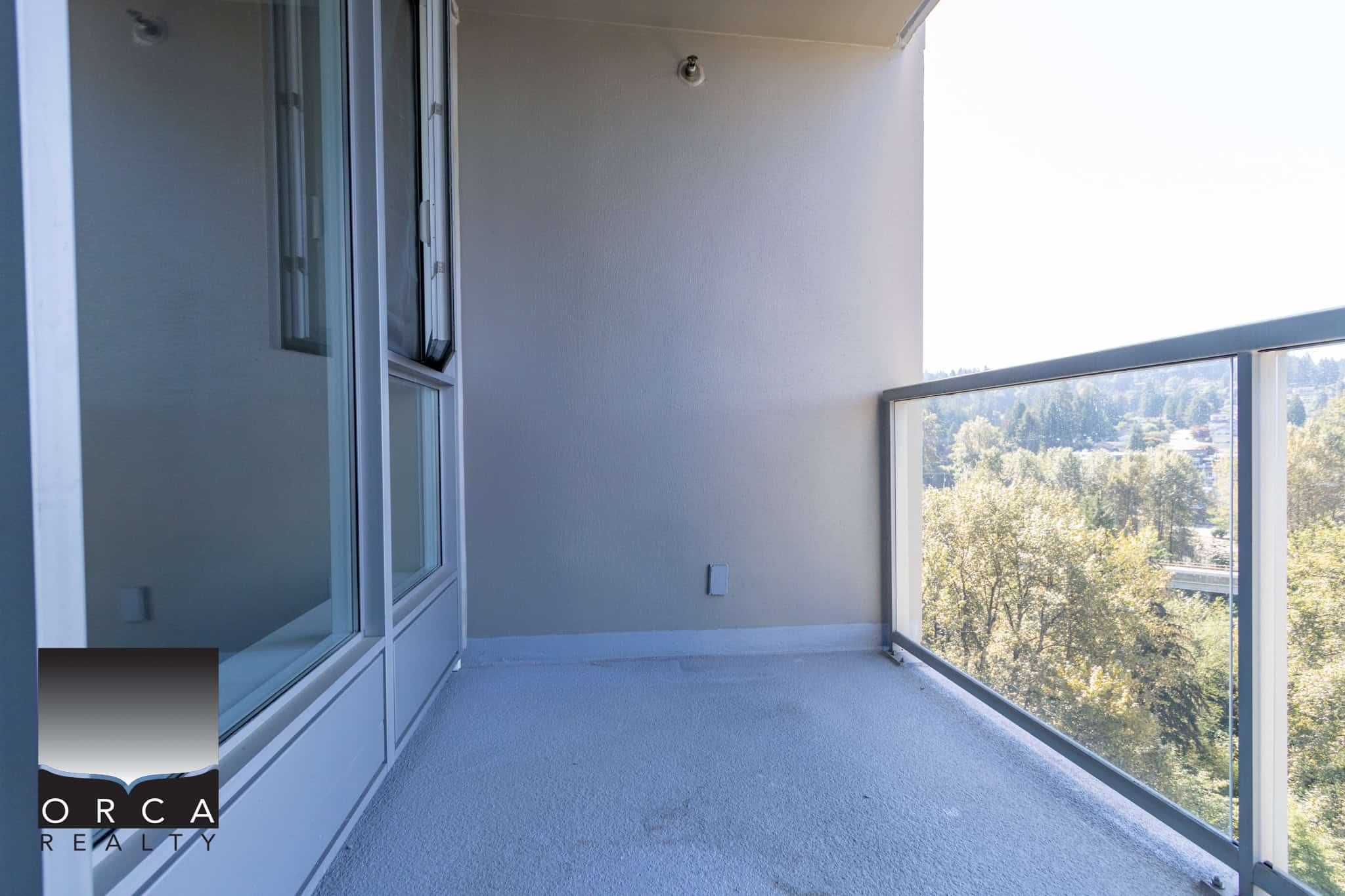 Balcony view in a modern apartment showcasing a glass railing and scenic greenery, perfect for enjoying outdoor living in Vancouver.