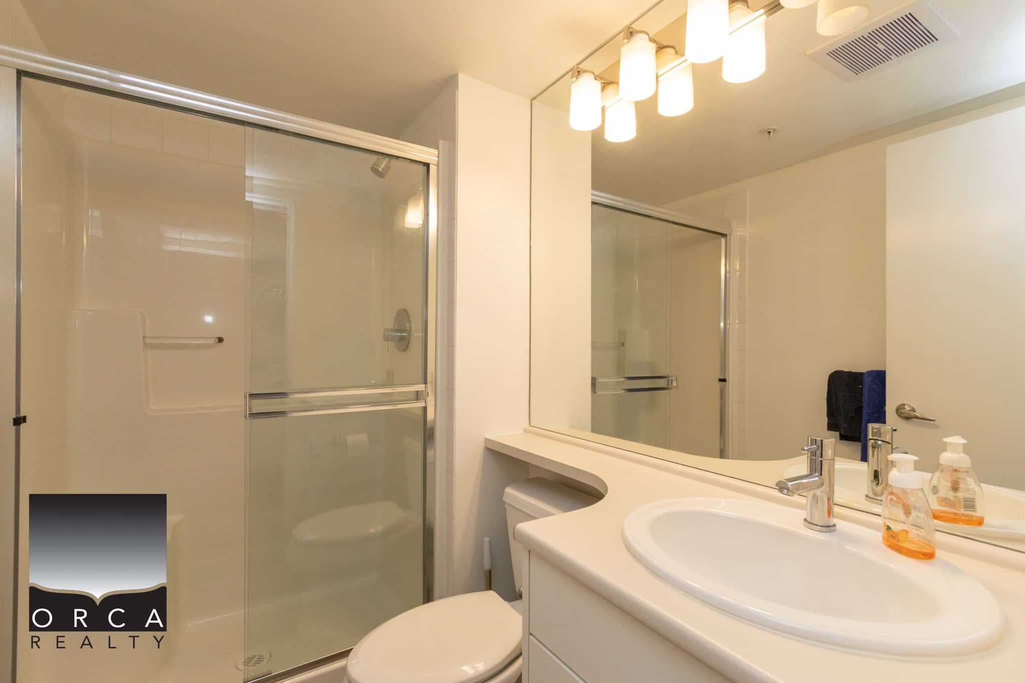 Modern bathroom with glass shower, white vanity, large mirror, and contemporary lighting, ideal for Vancouver real estate listings and showcasing properties for sale or rent.