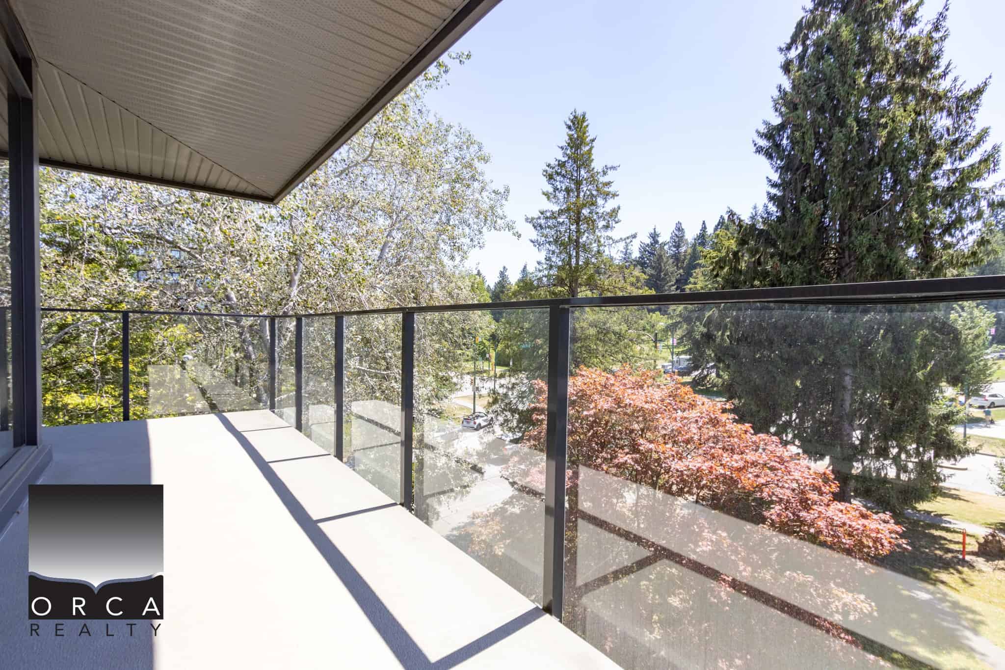 Spacious balcony with glass railing overlooking a lush green canopy, perfect for outdoor enjoyment and scenic views.