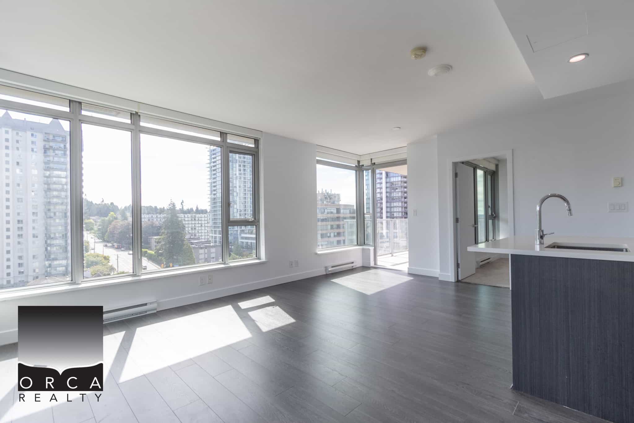 Bright and modern condo living space with large windows offering panoramic city views in Vancouver, BC. Featuring open-plan design, hardwood flooring, and contemporary kitchen, ideal for urban lifestyles.