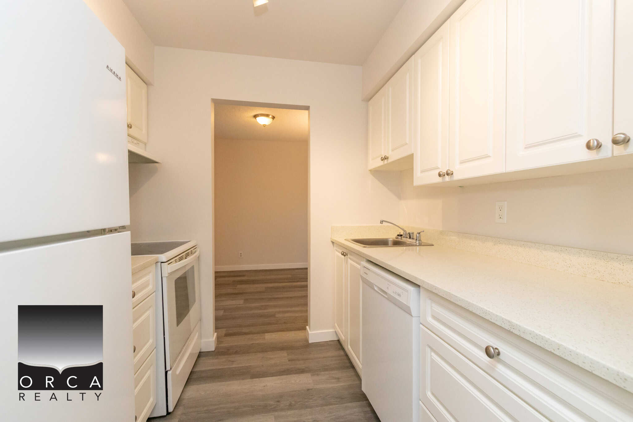 Bright white kitchen with modern cabinets and appliances, featuring a spacious countertop, stainless steel sink, and wood-like flooring, ideal for Vancouver real estate listings.