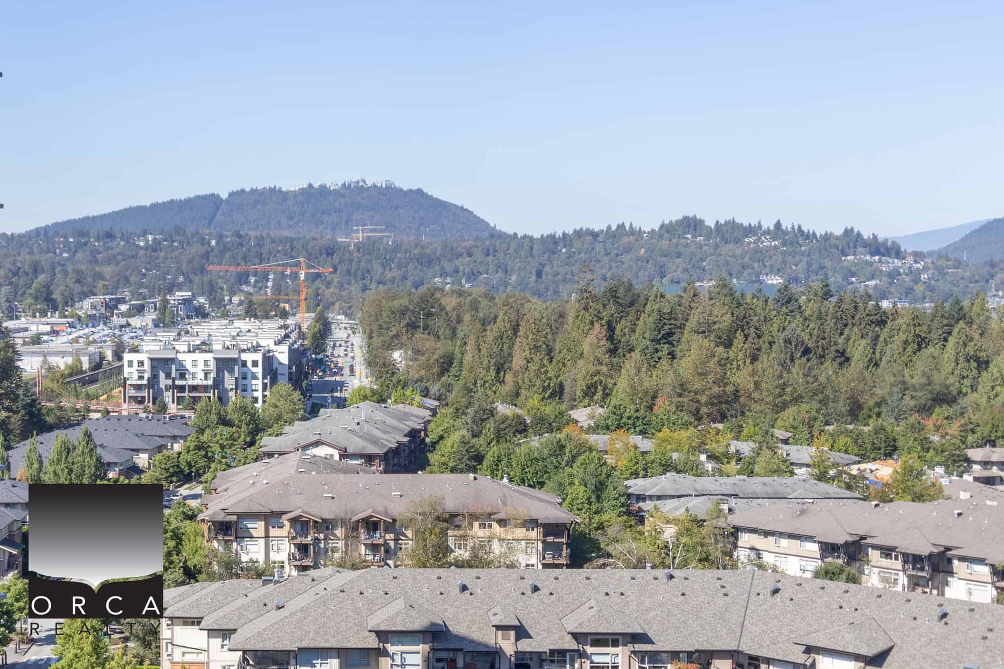 Panoramic view of suburban residential neighbourhood with modern apartment buildings, lush green trees, and mountainous backdrop in Vancouver, BC. Perfect setting for Buyers seeking real estate opportunities.