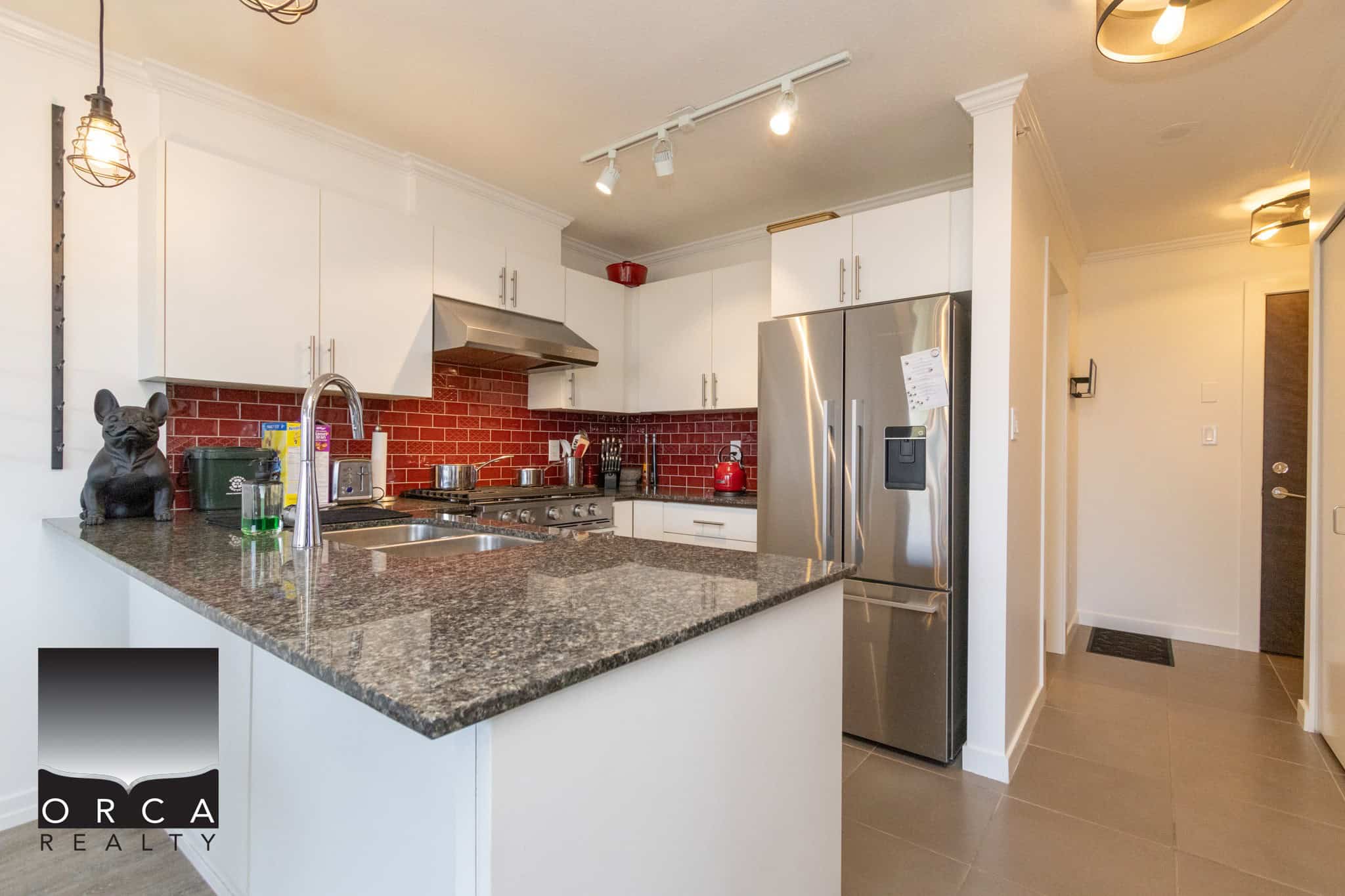 Modern kitchen with granite countertops, stainless steel appliances, and white cabinetry, featuring a red brick backsplash and contemporary lighting, ideal for Vancouver Island living.