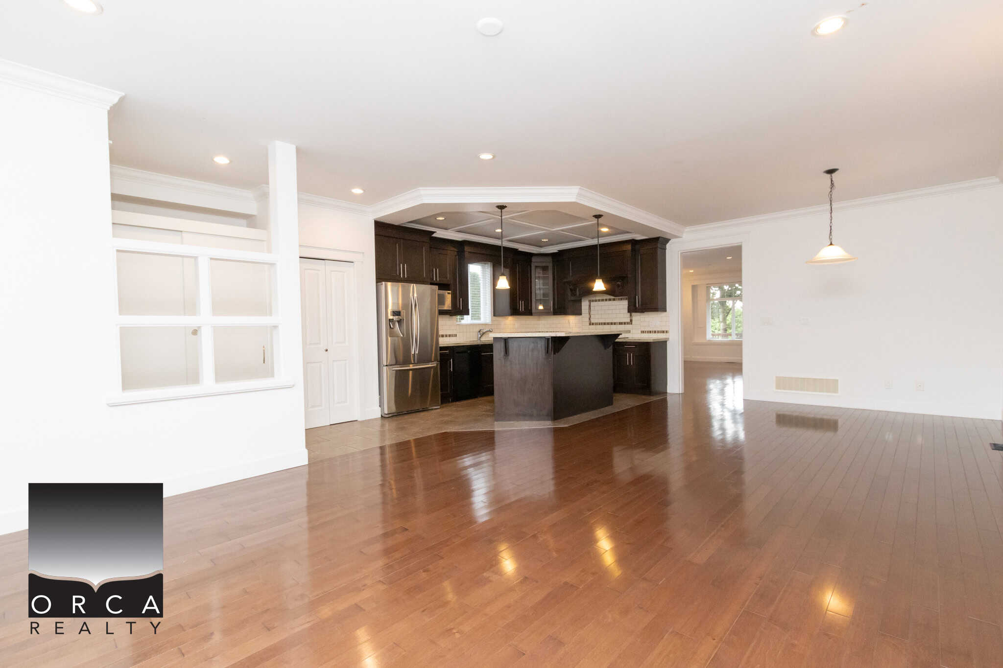 Bright open-concept kitchen and living space with dark wood cabinetry, stainless steel appliances, hardwood flooring, and modern lighting, perfect for Vancouver BC real estate buyers.