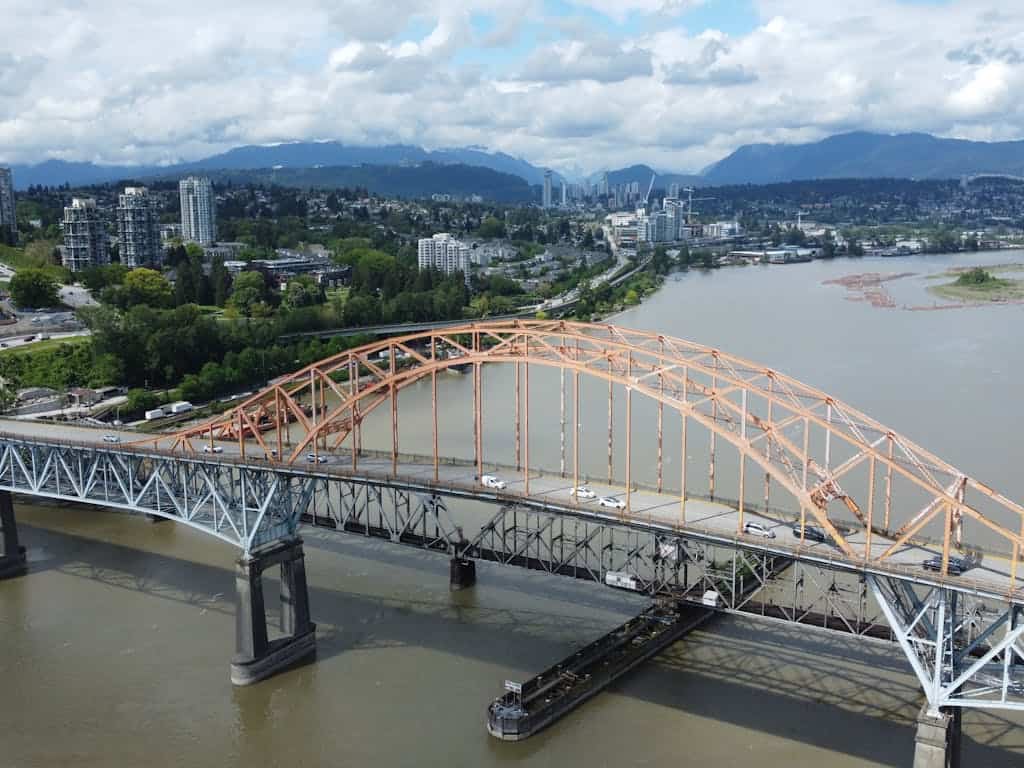 Elegant aerial view of a bridge over a river in Vancouver with city skyline and mountain backdrop, highlighting Western BC real estate opportunities with Orca Realty Inc.