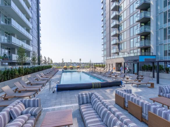 Modern apartment complex featuring a luxurious outdoor swimming pool with lounge chairs at Orca Realty Inc.