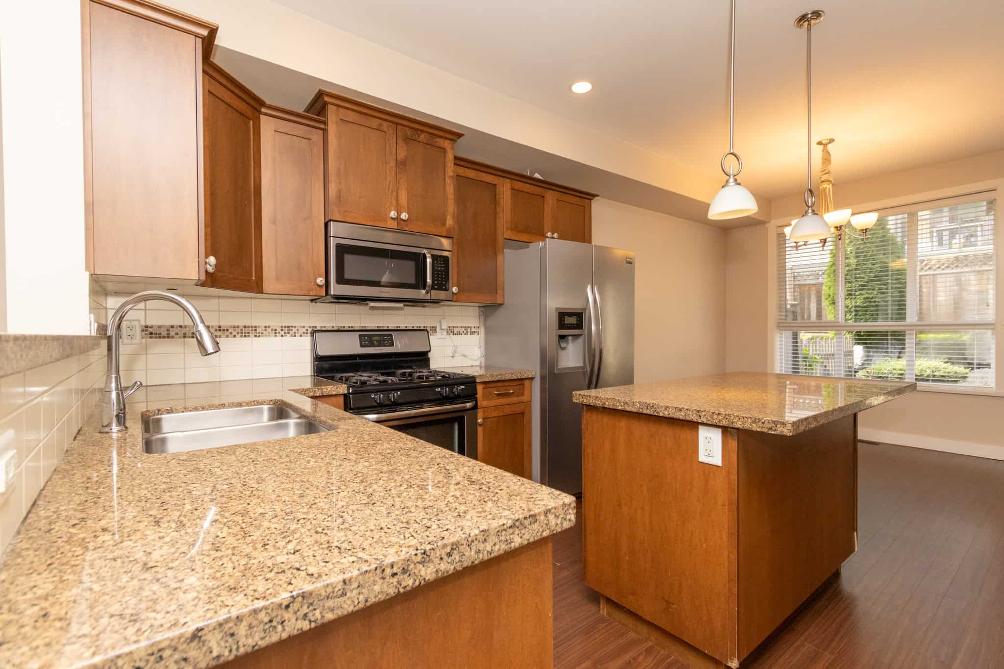 IMG_1787 Modern kitchen with granite countertops, wood cabinets, stainless steel appliances, and spacious island, perfect for homebuyers seeking stylish and functional Ontario real estate.