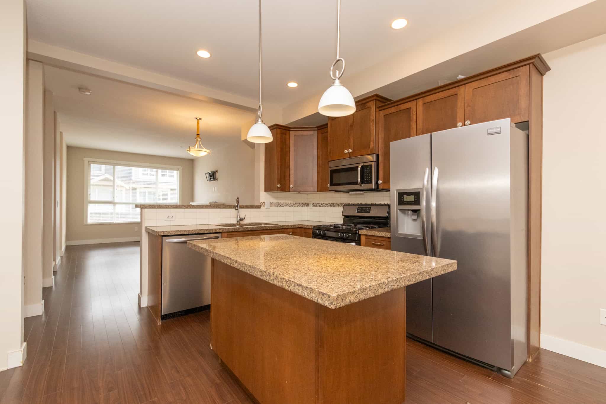 IMG_1790 Modern kitchen with stainless steel appliances and granite countertops, featuring warm wooden cabinets and ample space for family cooking and entertaining.