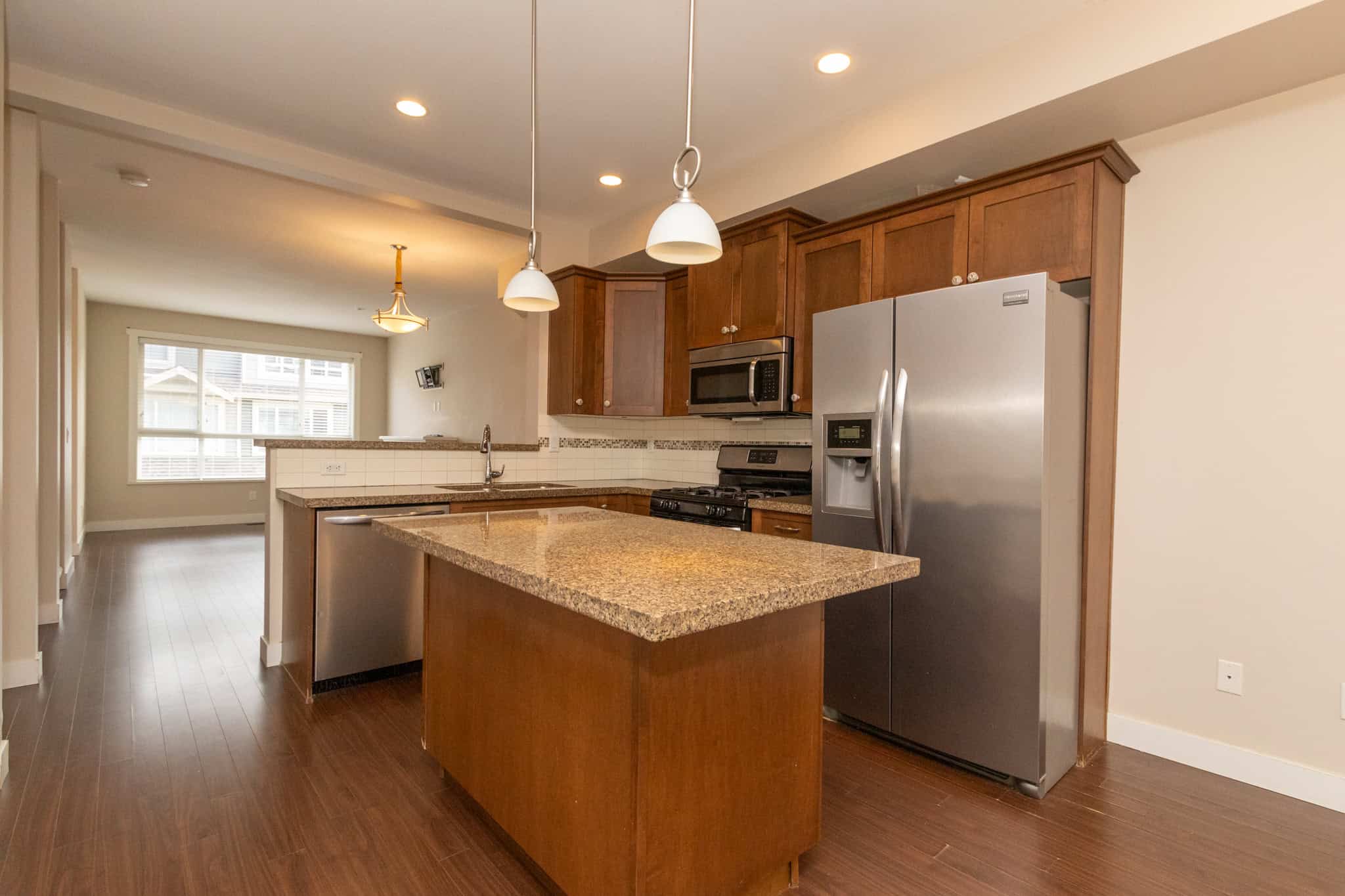 IMG_1803 Modern kitchen with stainless steel appliances, granite countertops, wooden cabinetry, and hardwood floors, featuring a spacious open-concept design in a residential home.