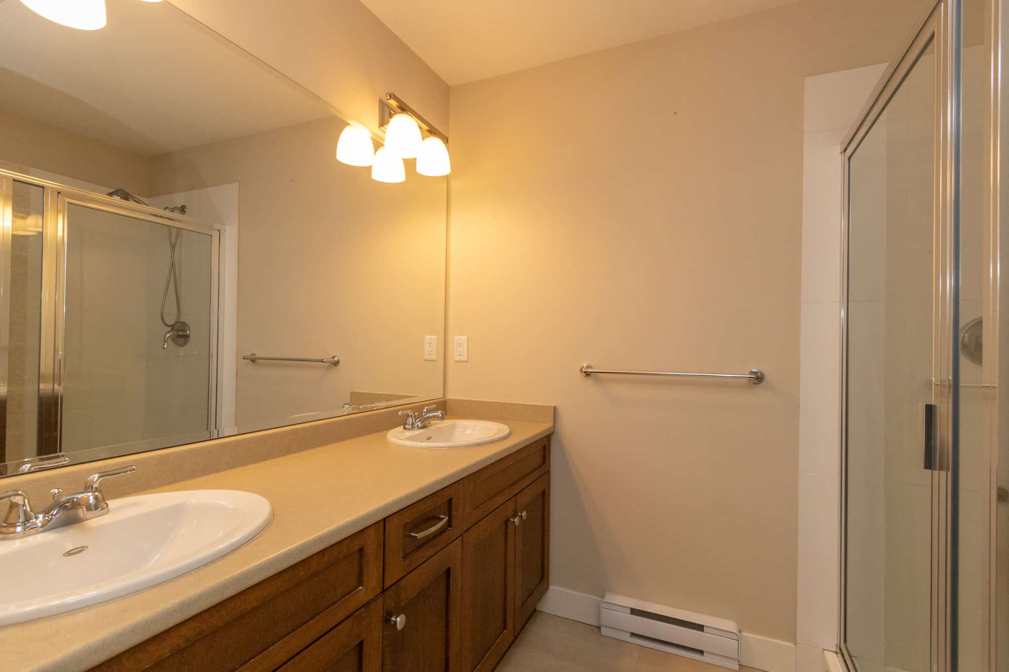 IMG_1809 Double sink bathroom vanity with large mirror and shower stall, neutral beige walls, updated lighting fixtures, and ample space, perfect for modern Vancouver Island homes.