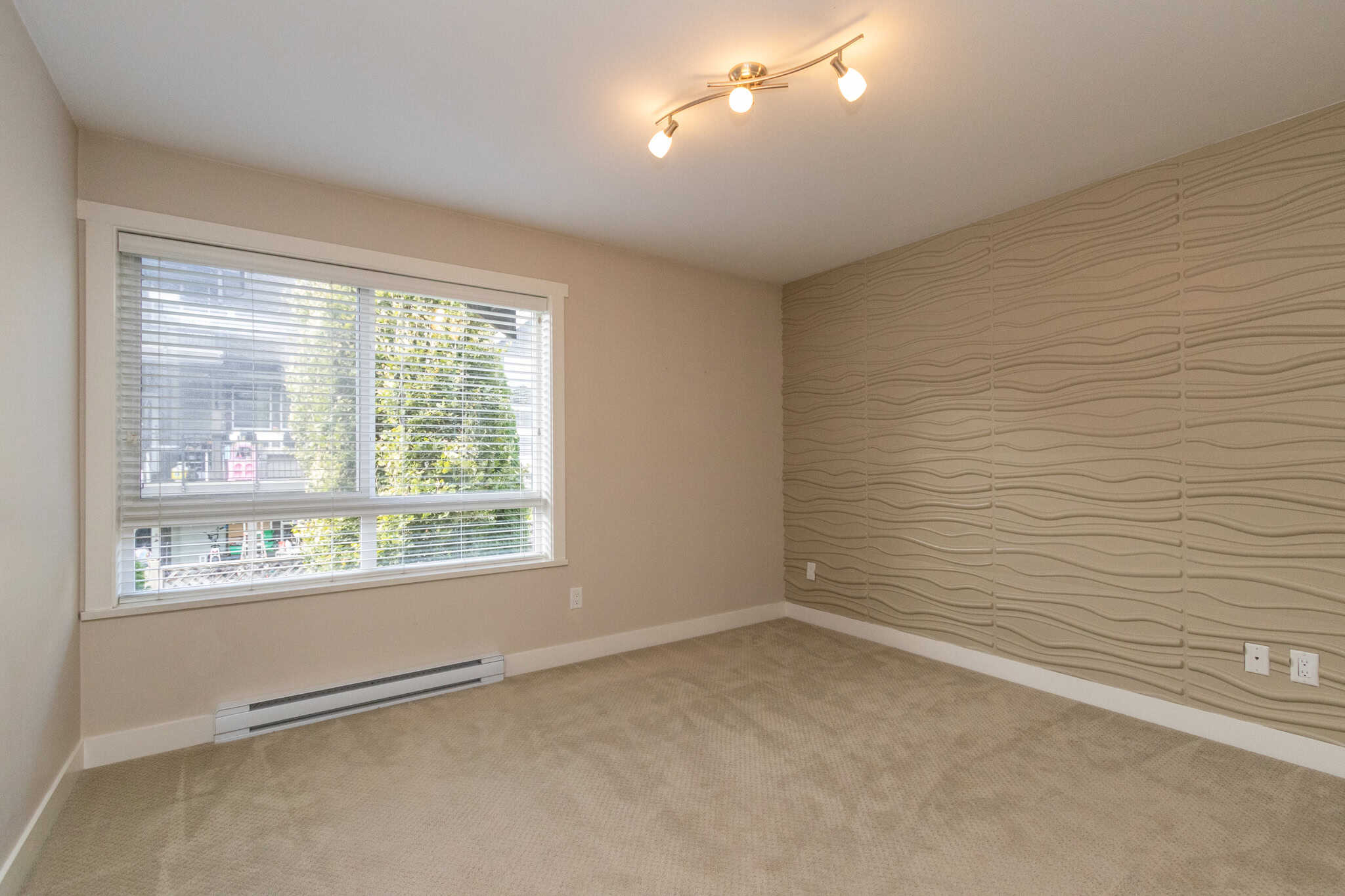 IMG_1811 Spacious empty living room with large window and textured accent wall in a modern condo, showcasing bright natural light, neutral tones, and clean design for Vancouver real estate.