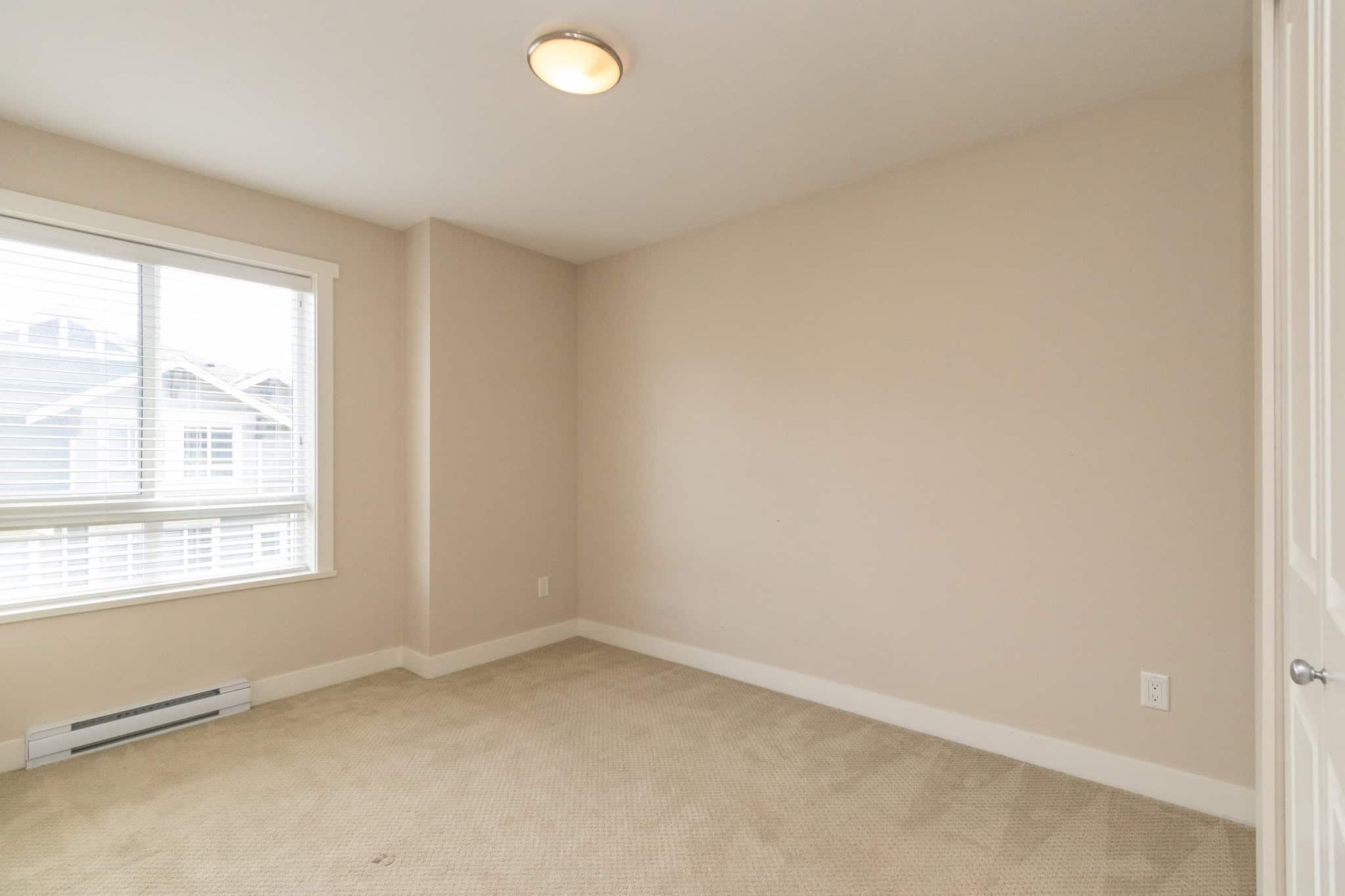 IMG_1816 Bright empty bedroom with large window, beige carpet, neutral walls, and ample natural light, ideal for Vancouver home buyers seeking cozy, move-in ready residential spaces.