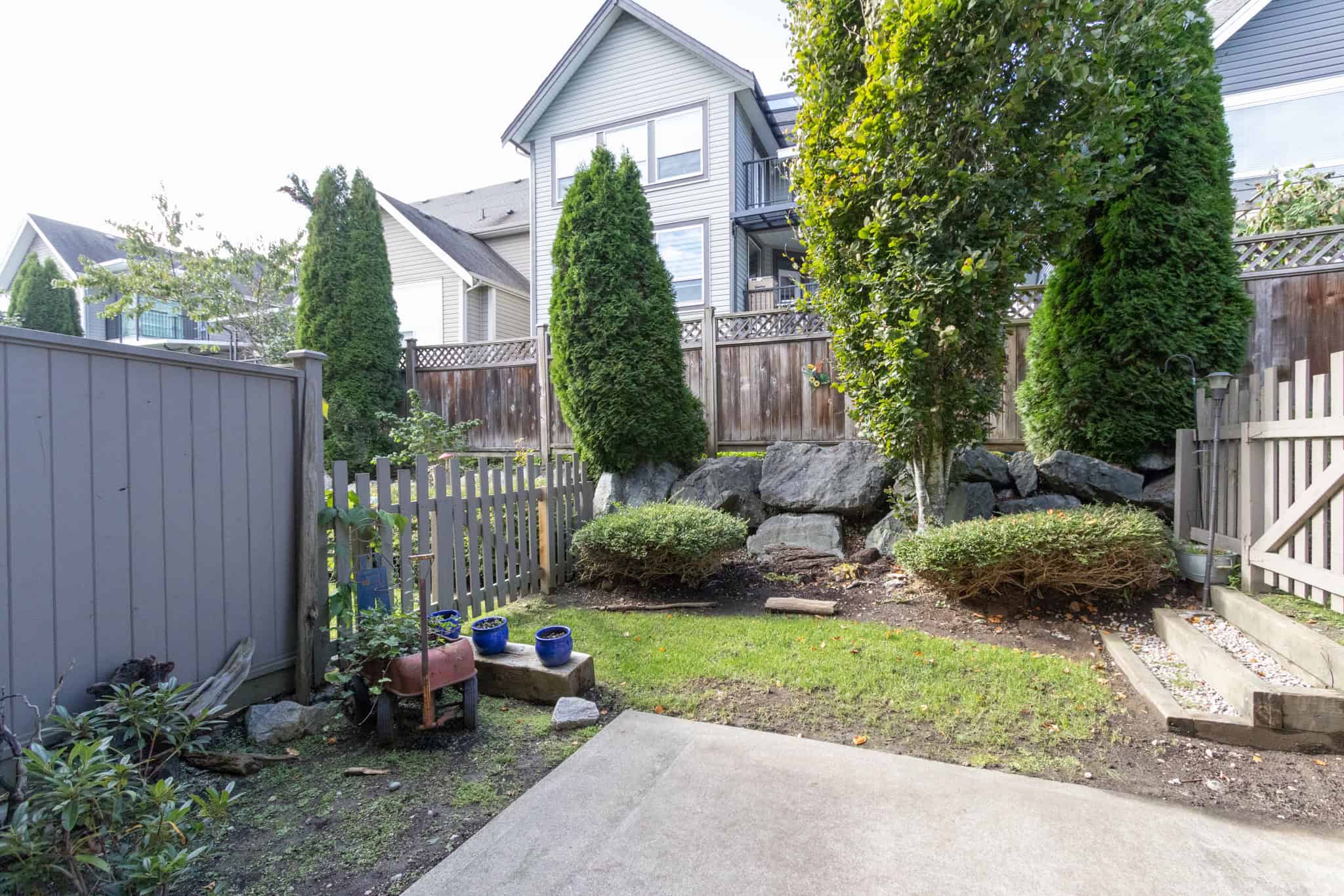 IMG_1830 Lush private backyard with mature trees, decorative rocks, and a small patio area, ideal for outdoor living and gardening.