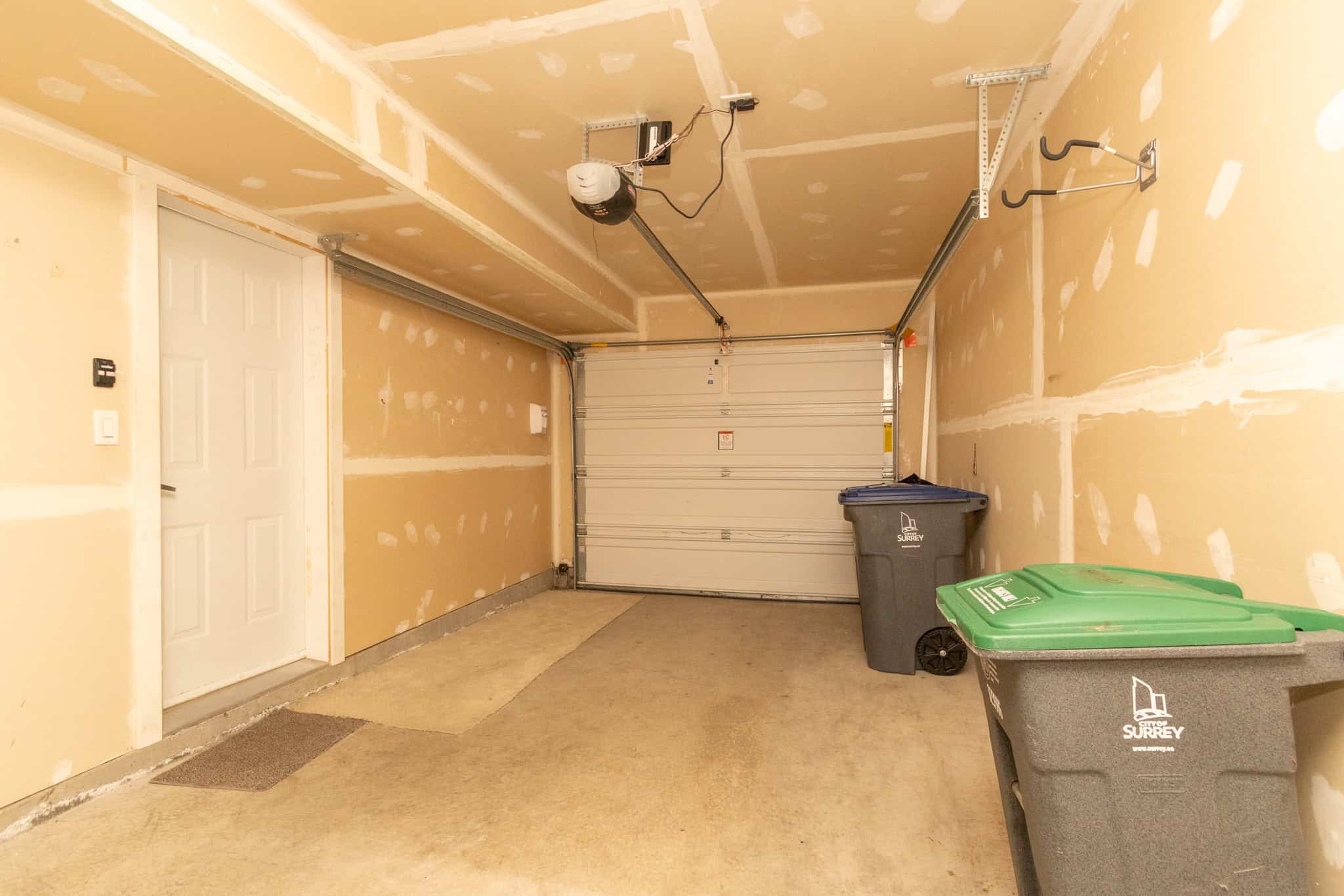 IMG_1843 Spacious garage with unfinished drywall, concrete flooring, and storage bins, ideal for residential or commercial property storage solutions in BC.