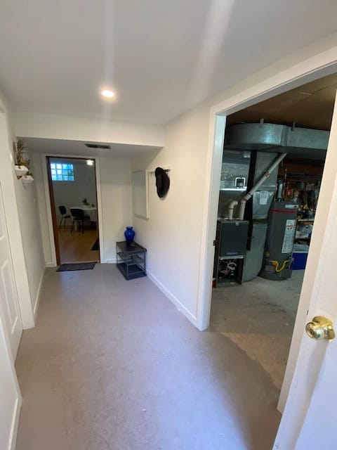 Bright interior hallway in a residential property showcasing the entry to a utility room with HVAC equipment, featuring white walls, neutral carpet, and a minimalist decor decor.