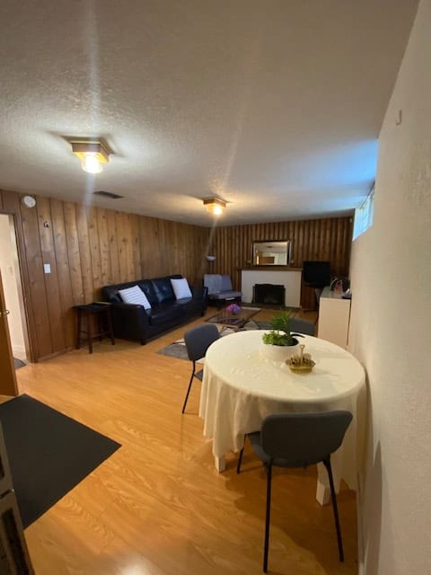 Living room with wood-paneled walls, black sofa, and cozy fireplace, featuring a small dining area with a round table and three chairs, perfect for family gatherings or entertaining guests.