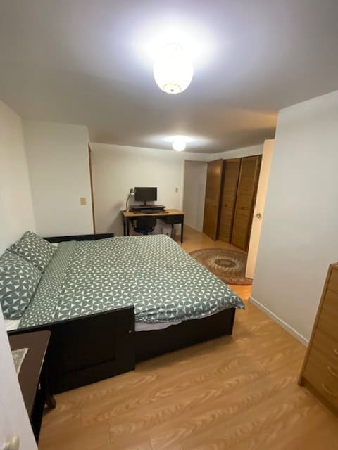 Cozy bedroom with wooden flooring, bed with patterned bedding, desk with computer, and large closet, showcasing Vancouver Island real estate opportunities.