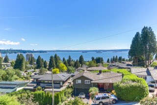 Orca realty inc Vancouver waterfront view of homes and lush greenery in a residential neighborhood with mountains and water in the background.