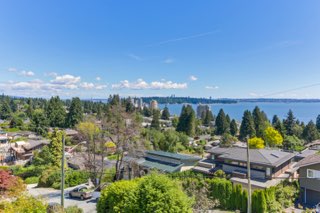 Panoramic view of a Vancouver suburban neighborhood with lush greenery, water, and city skyline in the background, showcasing real estate opportunities in British Columbia.