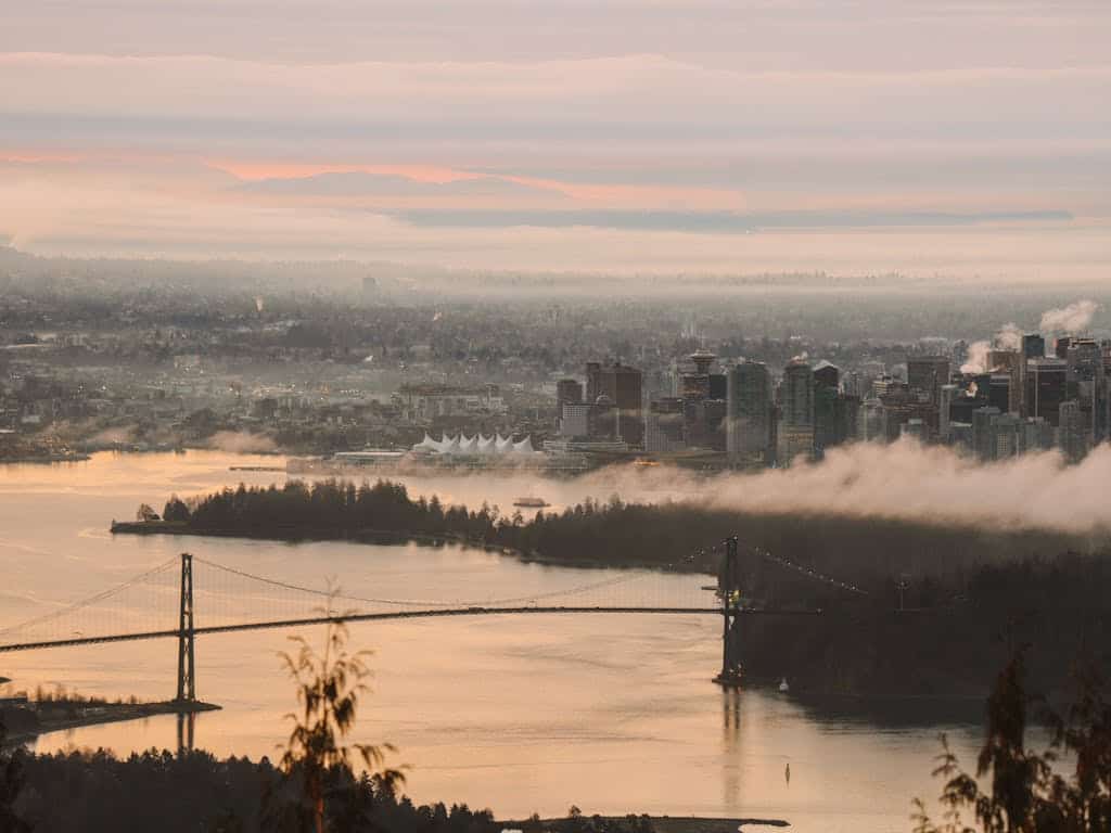 Vancouver city skyline with Lions Gate Bridge, fog, and a pink sunset sky, showcasing scenic views and real estate opportunities in Vancouver, British Columbia.