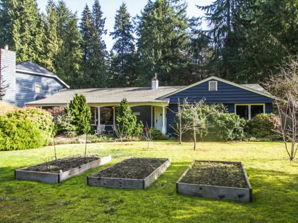 Lush backyard garden of a charming house with raised vegetable beds, surrounded by mature trees and well-maintained landscaping, perfect for outdoor living and gardening.