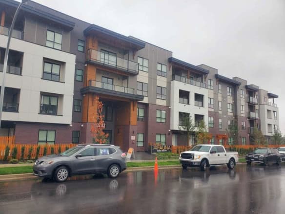 Contemporary multi-family residential apartment building with modern architecture, balconies, and a landscaped frontage on a rainy day in Vancouver, BC.
