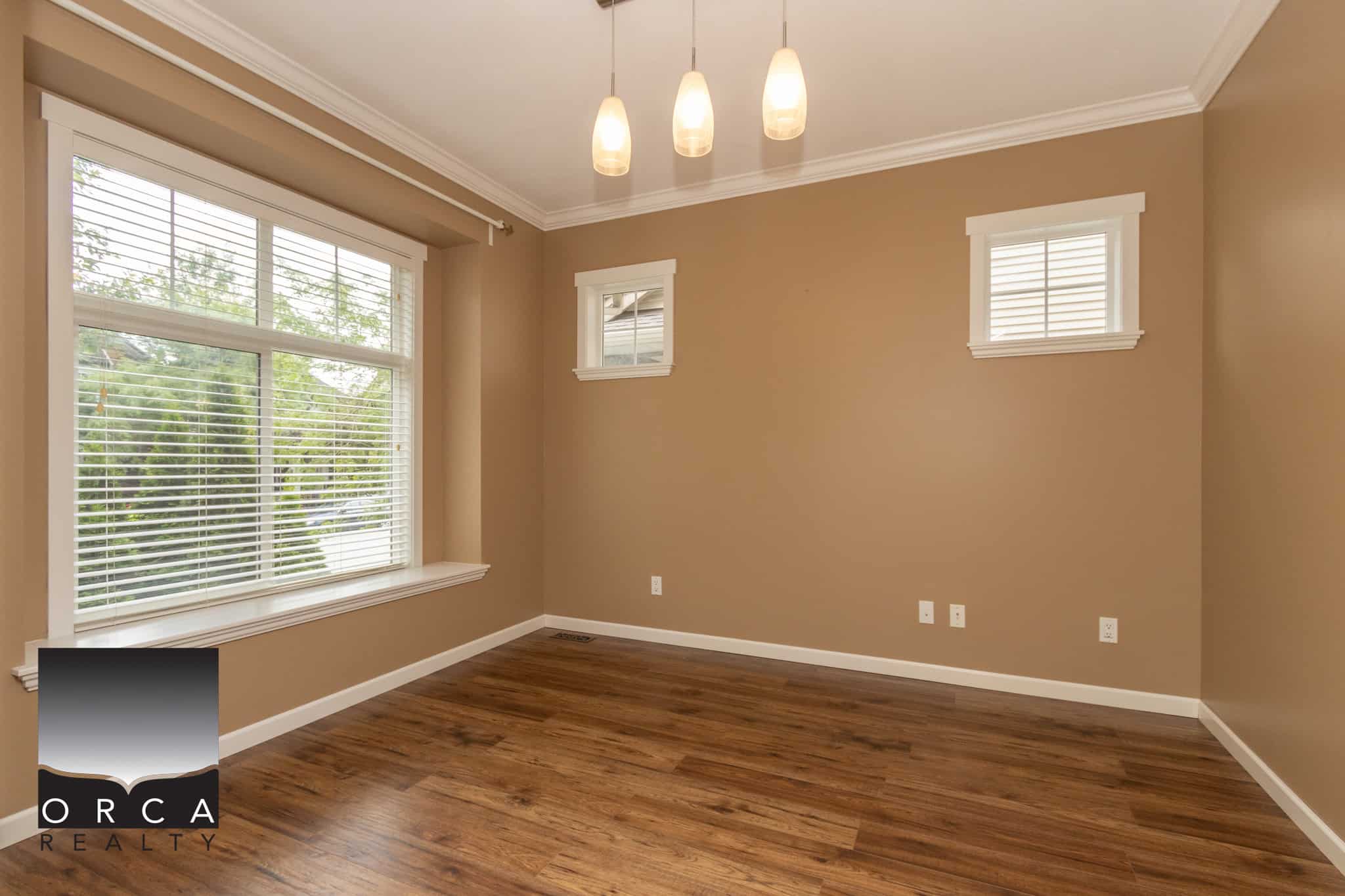 Bright empty living room with large window, beige walls, white trim, hardwood floor, and modern lighting fixture, ideal for home staging or real estate listings in Vancouver.
