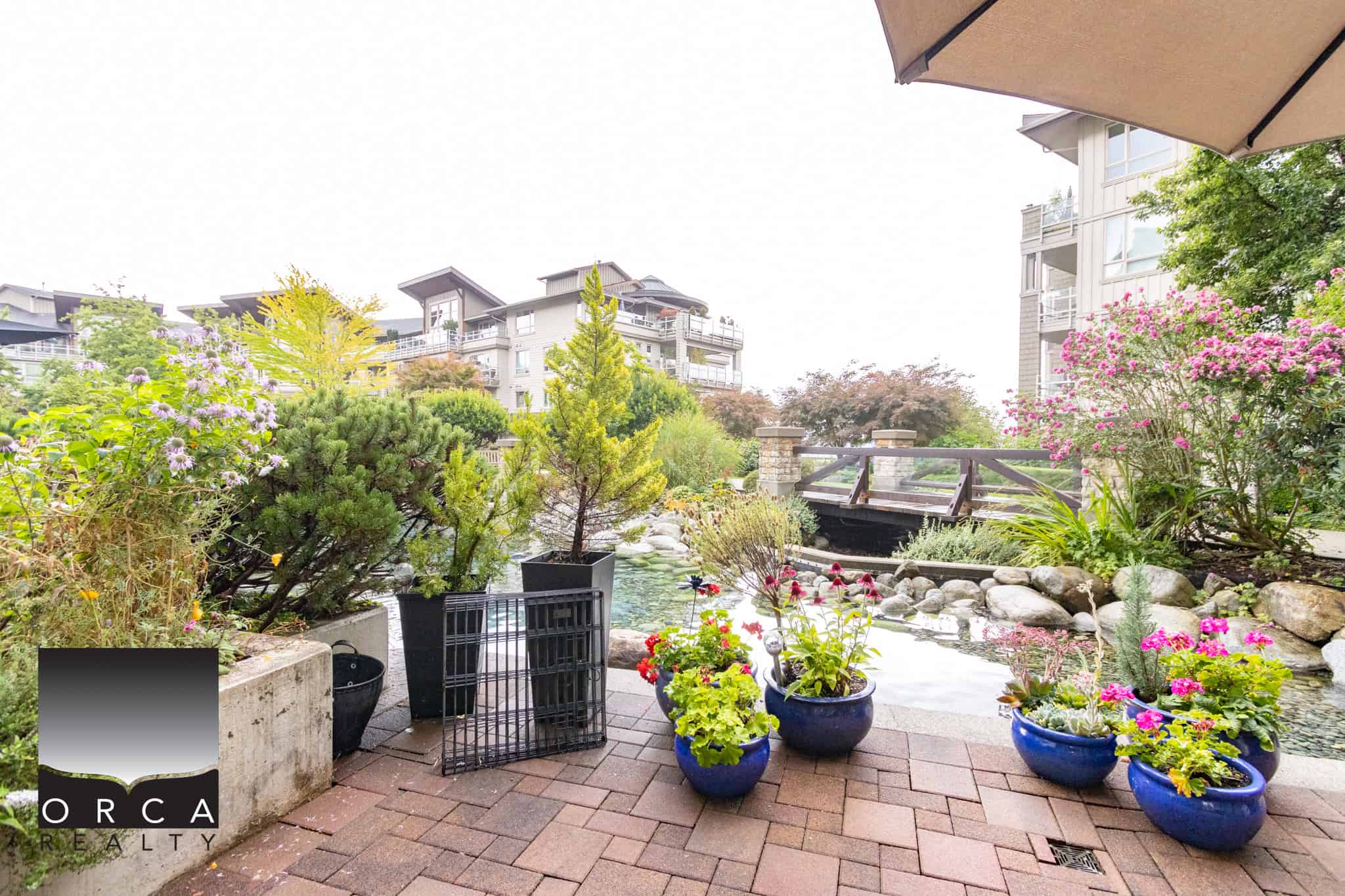 Lush garden with potted plants and a small stream at Orca Realty Inc., showcasing beautiful landscaping and outdoor spaces in Vancouver, perfect for homebuyers seeking natural serenity.