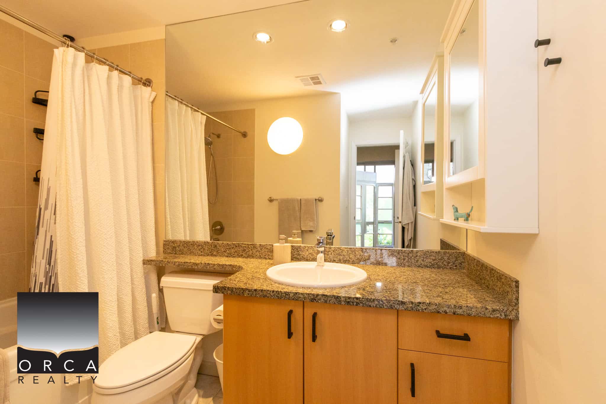Bright modern bathroom with beige tiled shower area, white curtains, granite countertop vanity, and natural light from a nearby window, showcasing stylish and functional Vancouver real estate.
