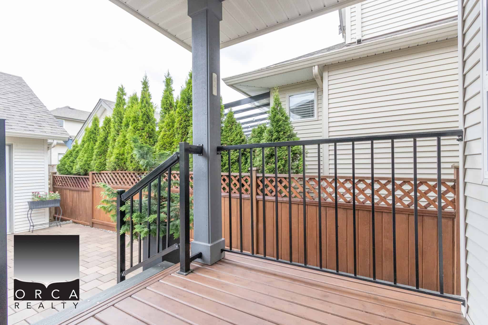 Modern backyard deck with black metal railing, surrounding lush evergreen trees and privacy fencing, ideal for outdoor living and entertaining.