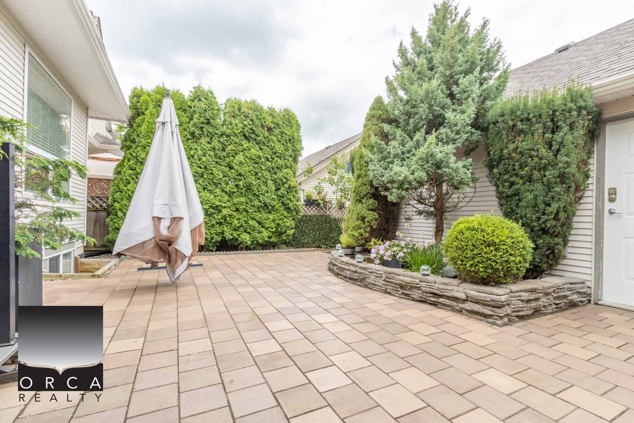 Lush backyard patio with mature trees and landscaped garden beds, perfect for outdoor living and entertaining. A private, serene space ideal for family gatherings and enjoying Vancouver Island's natural beauty.