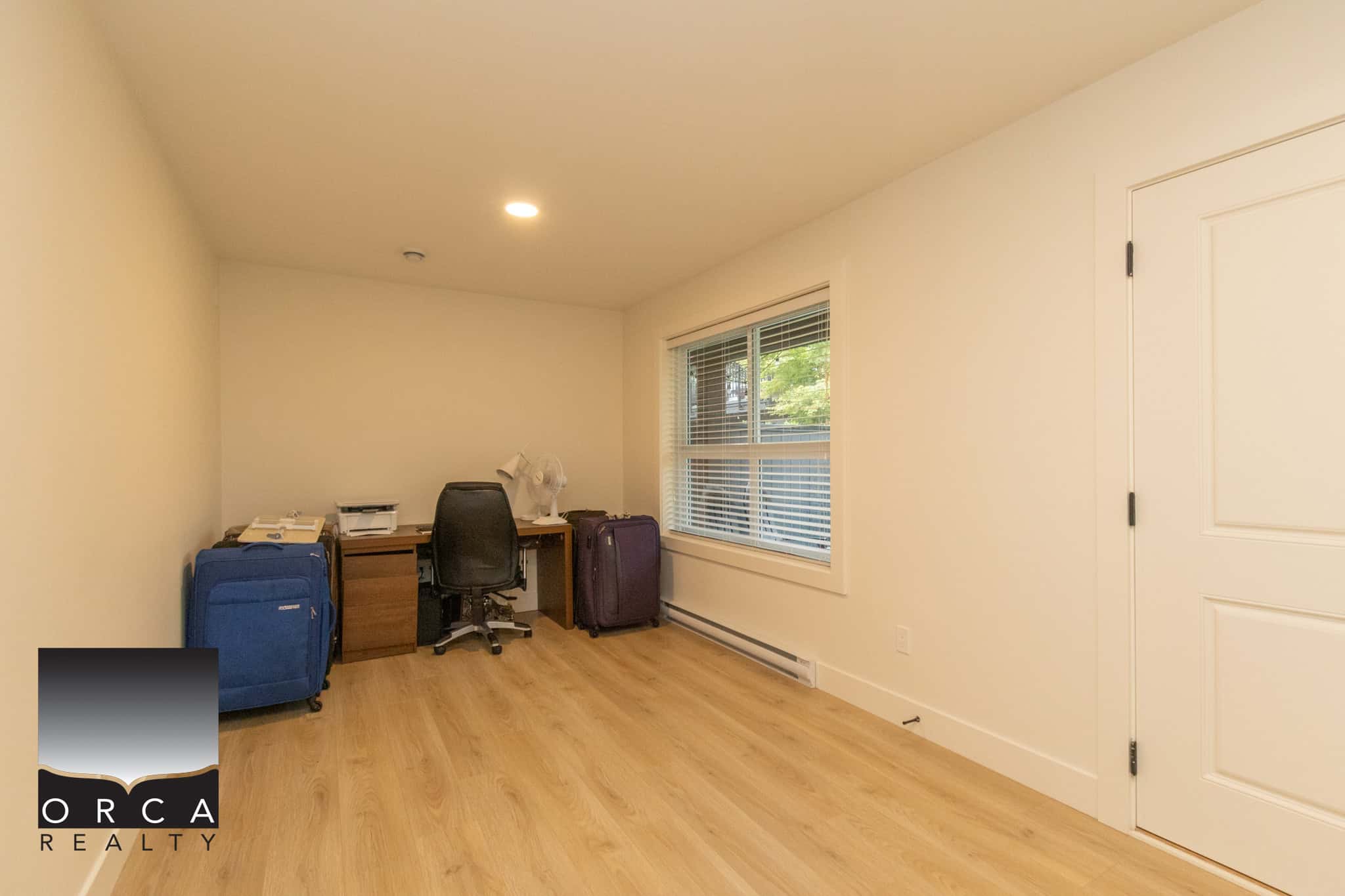 Bright home office with natural light, hardwood floors, and neutral walls, perfect for remote work or study, featuring a desk, chair, and luggage storage, ideal for residential or investment property listings.
