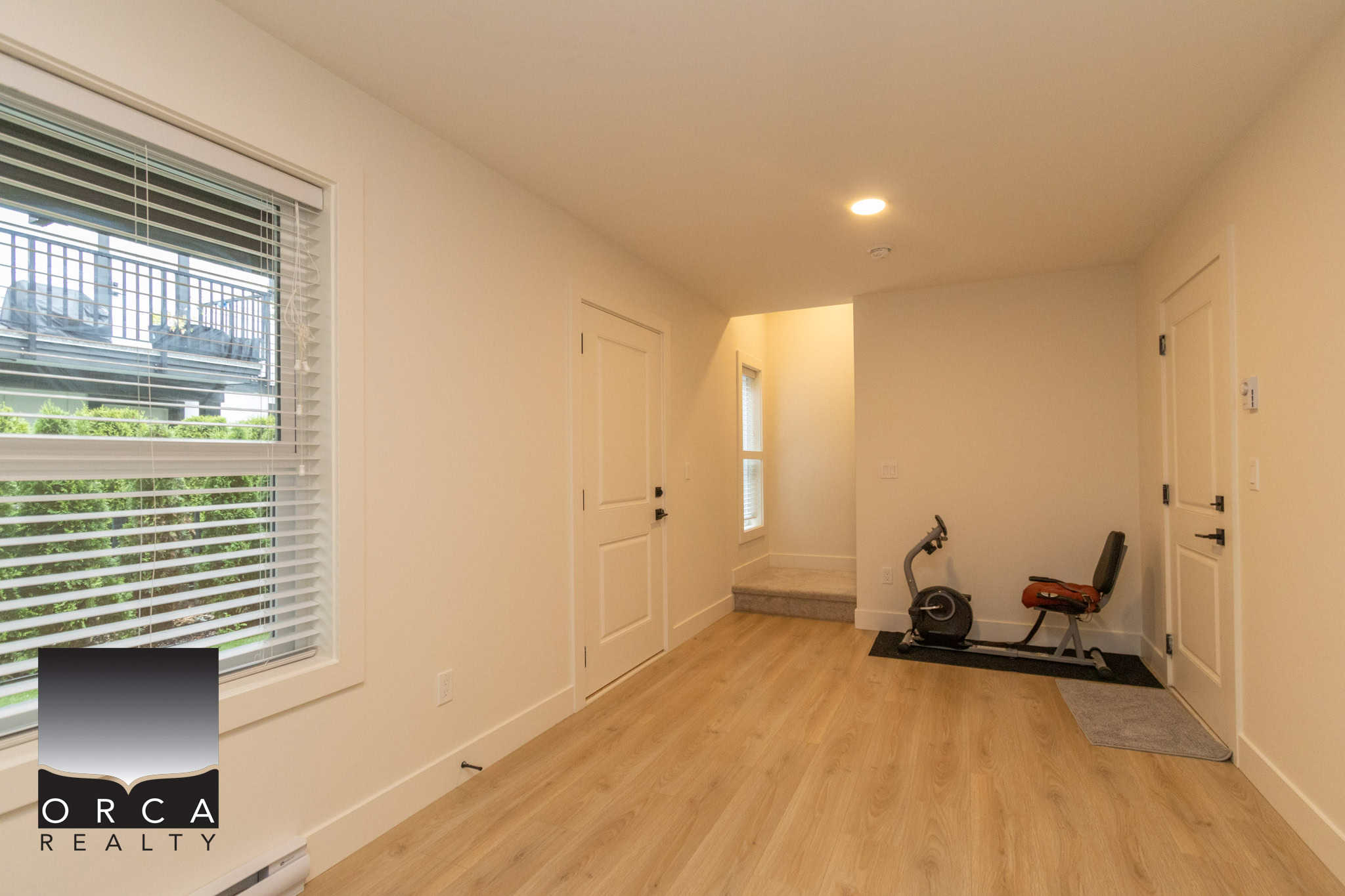 Modern interior of a residential property with cream walls, hardwood flooring, large window with blinds, and minimal furnishings, showcasing a clean, inviting living space ideal for real estate listings.