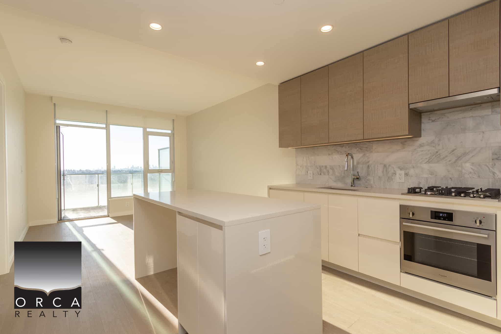 Bright modern kitchen with white cabinetry, stainless steel appliances, marble backsplash, and spacious island in a new condo with large windows and balcony views.