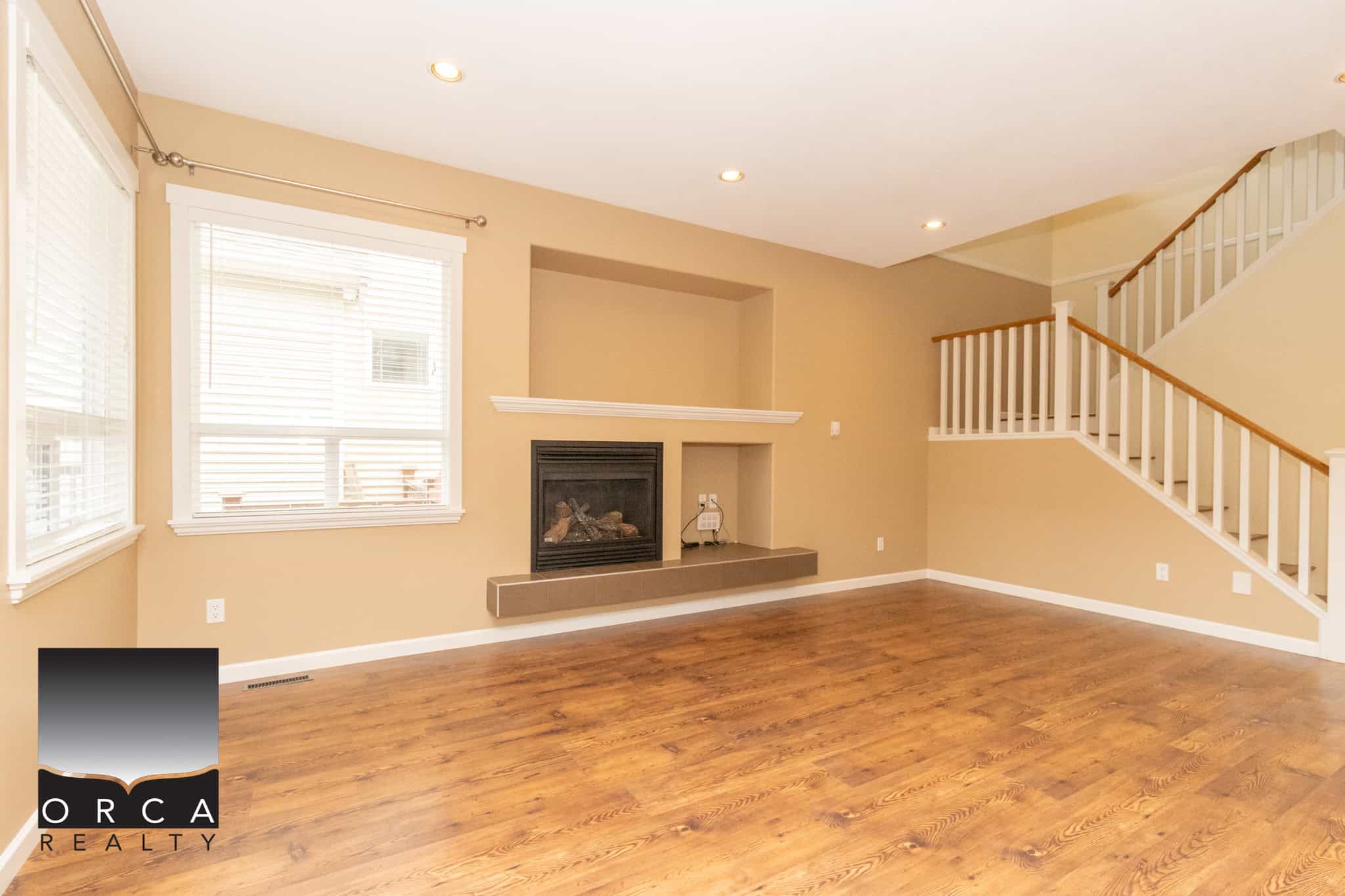Bright open living room with hardwood flooring, large windows for natural light, and a cozy fireplace, perfect for family gatherings and showcasing in Orca Realty property listings.