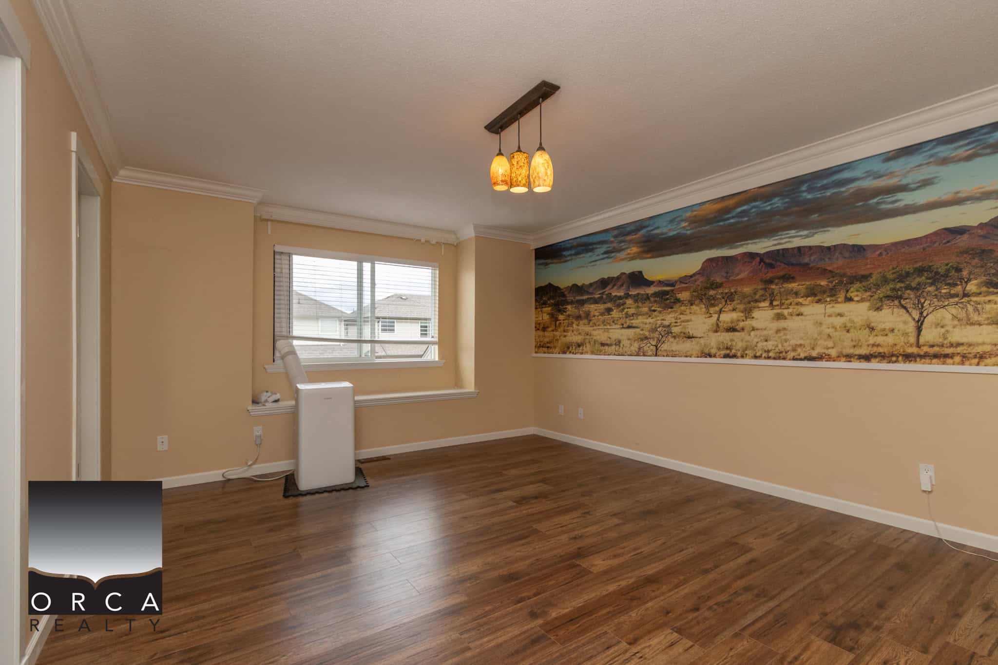 Spacious living room with warm beige walls, a stunning landscape mural, hardwood flooring, and large window providing natural light perfect for homebuyers and real estate listings.