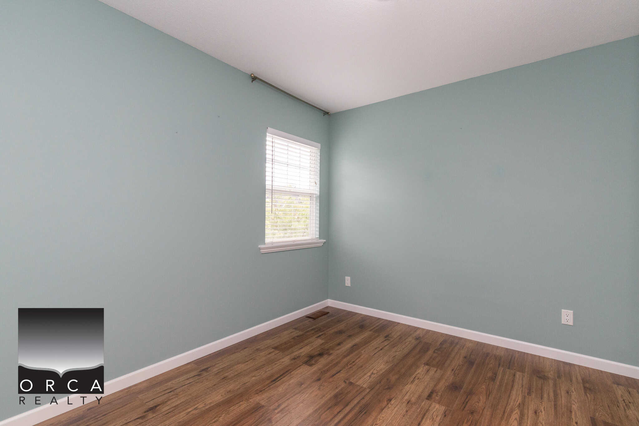 Bright empty room with soft blue walls, hardwood flooring, natural light from window, perfect for home staging and real estate listings in Vancouver.