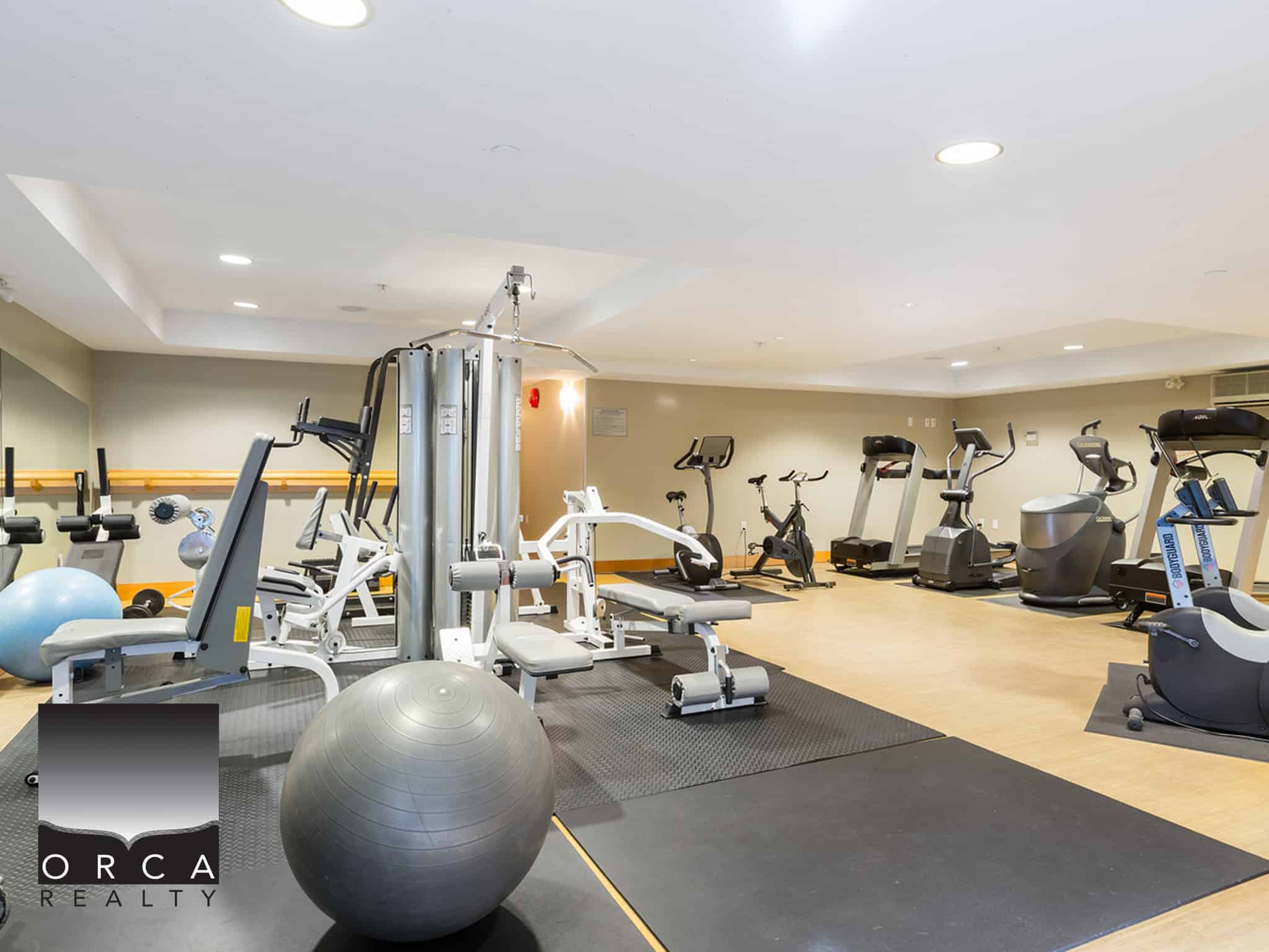 Modern gym for fitness and wellness at Orca Realty Inc. featuring exercise equipment, cardio machines, and strength training options in a spacious, well-lit environment.